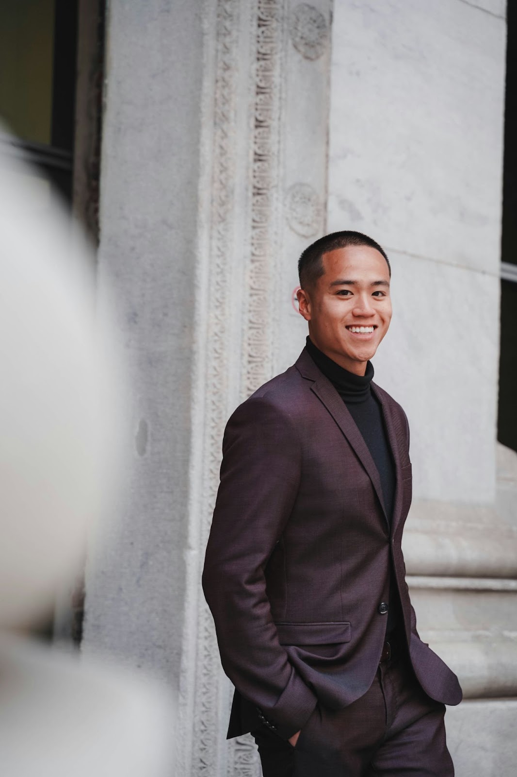 A guy in a suit is giving a side pose for his realtor headshots. He is smiling warmly to seem approachable to his clients.