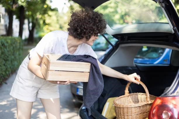 Young woman packing and preparing for a picnic Portrait of a beautiful young woman packing a box and a basket into a car trunk and preparing for a picnic Roof basket for your road trip stock pictures, royalty-free photos & images