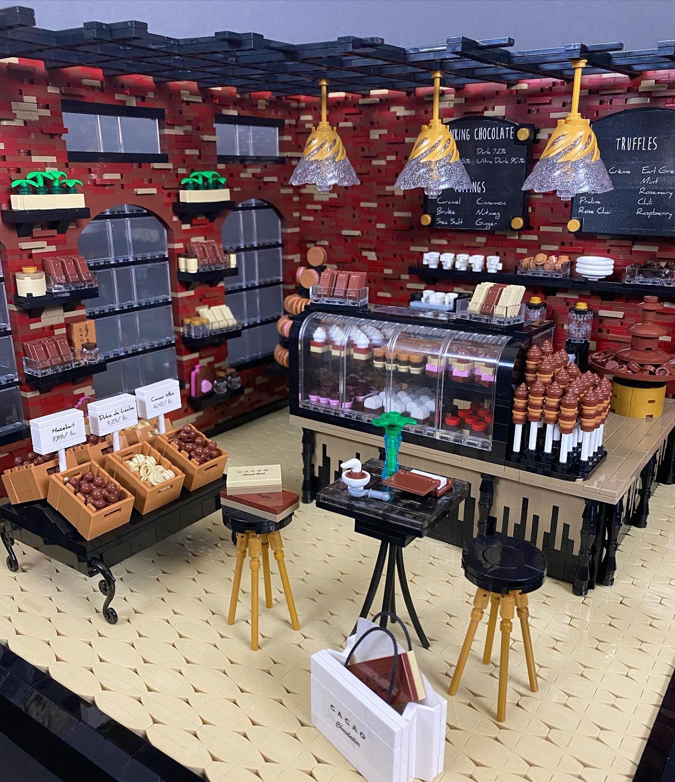 A photo of the LEGO creation Chocolate Shop, by Kelly Bartlett, depicting a colorful store interior with sweets of many different types in bins and behind display cases, plus menus, lamps in the ceiling, stools, and a table