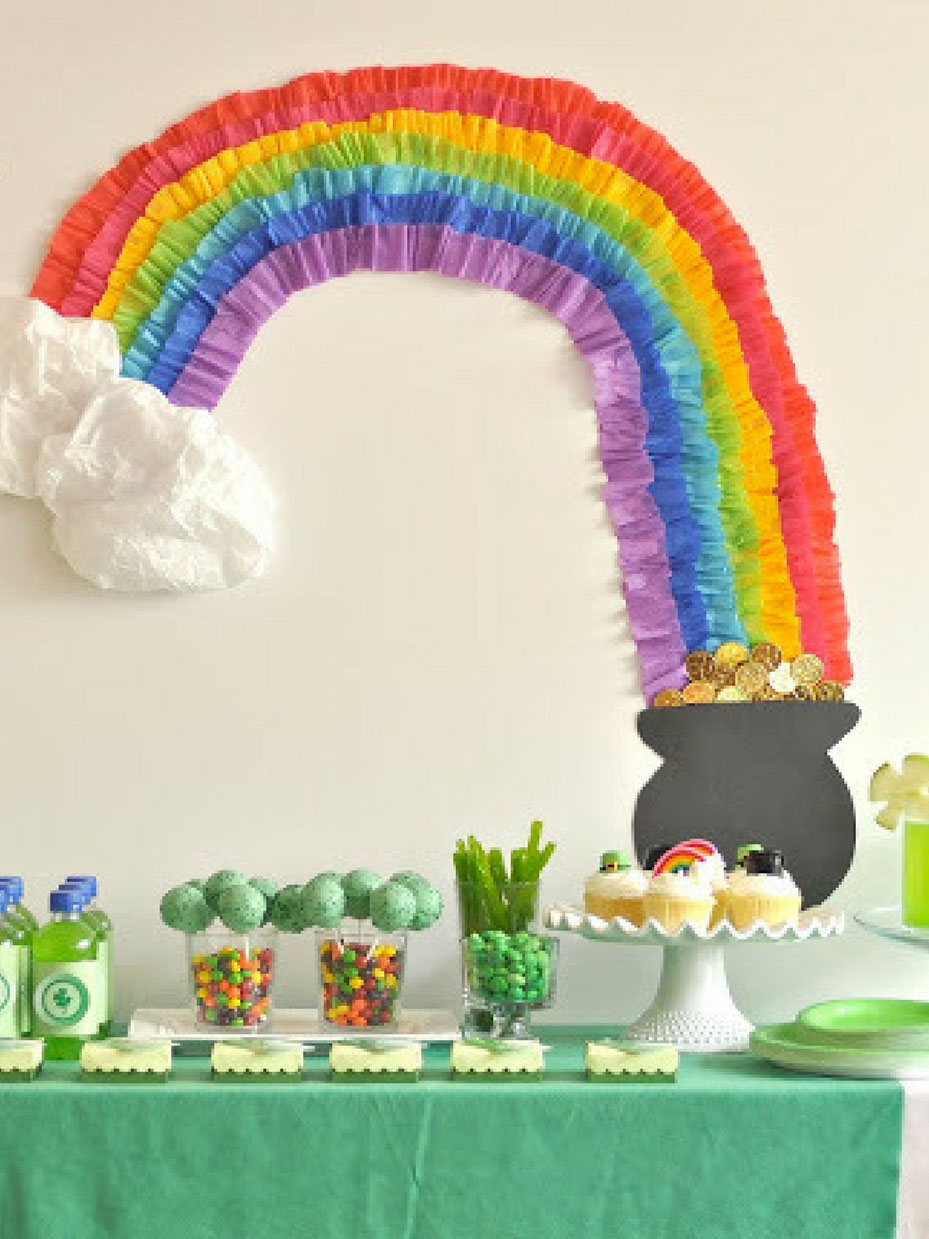 Rainbow made out of tissue paper going into a pot of gold decoration on the wall behind of a table of food