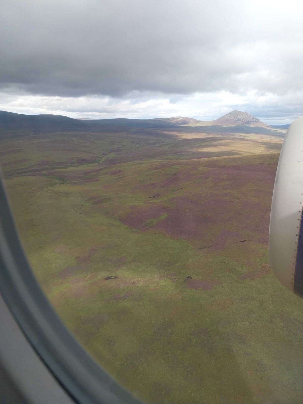 Scottish moorlands viewed from the window of a large aircraft that is flying over at low altitude. The edge of an engine is visible.