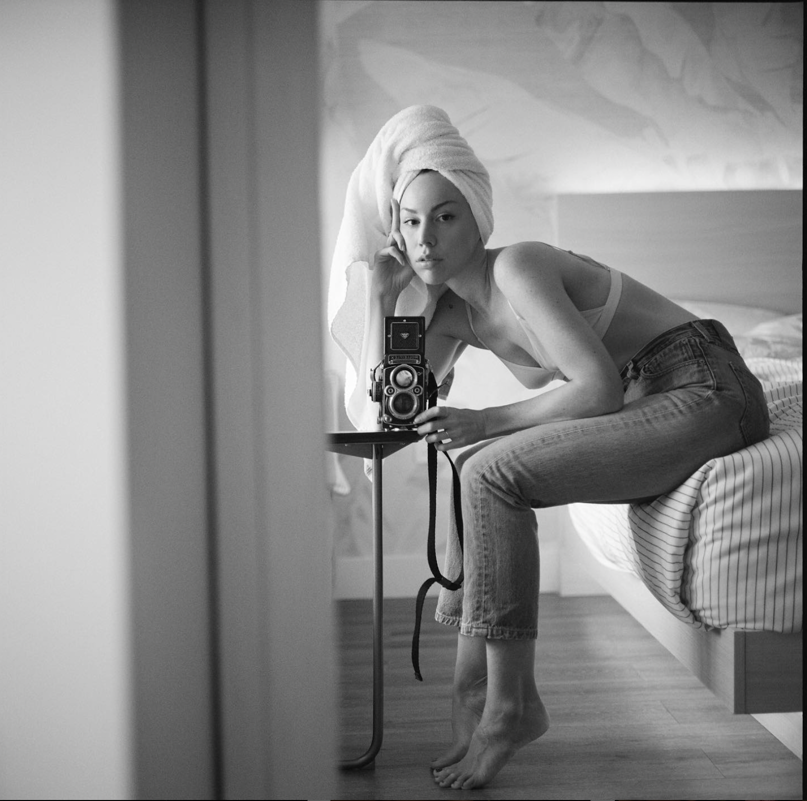 A self portrait of Allister Ann, her sitting on a bed looking into a mirror leaning over a vintage camera. 