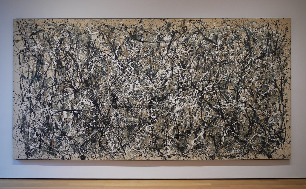 An image of a Jackson Pollock painting hanging in a gallery. The painting is splashed with organic, monochromatic strokes of paint.