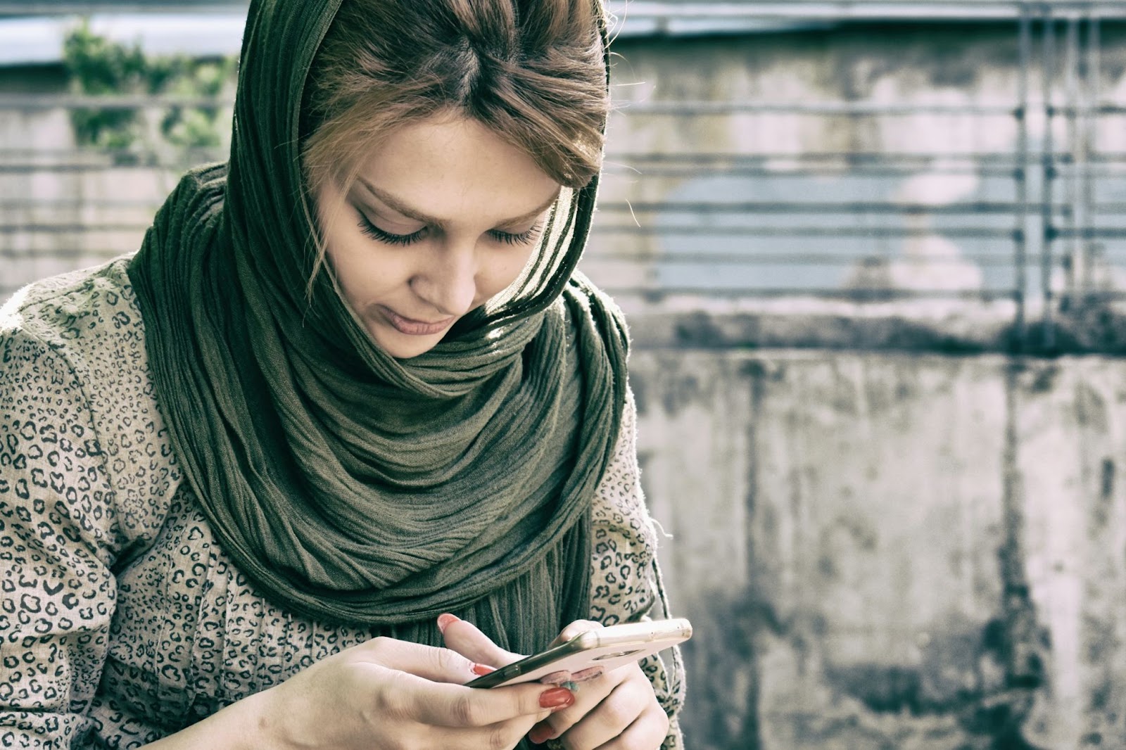 Woman walking through town wearing a hijab while looking at her smartphone.