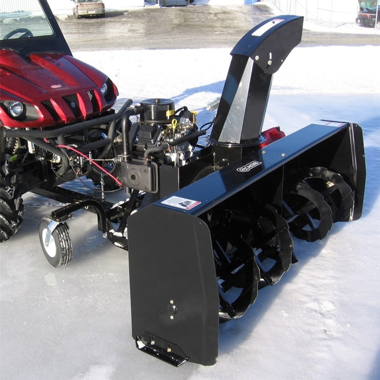 A front-oblique view of a Honda Pioneer Versatile Snowblower by Bercomac, installed on a side-by-side and in use over snowy terrain.