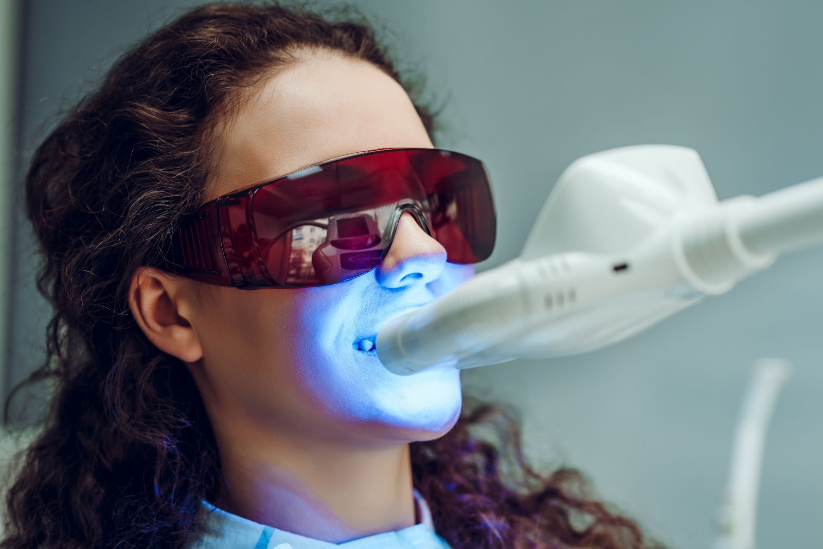 A woman having her teeth professionally whitened with LED lights at the dentist