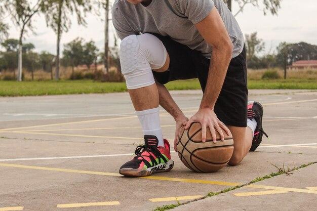 Photo detail shot of a young man holding a ball while kneeling on an abandoned basketball court.