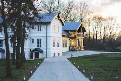 Elegant white house with a covered porch at dusk, end of a gravel driveway.