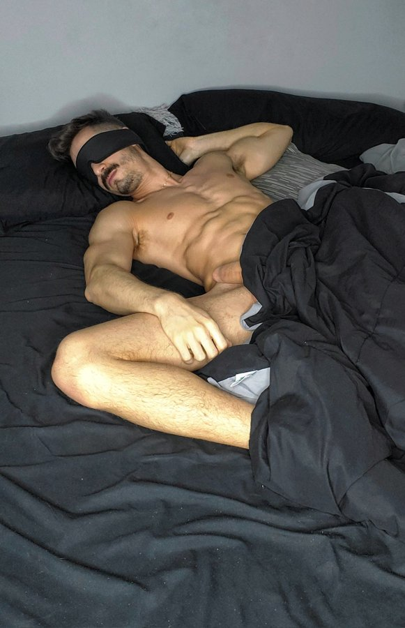 william miguel lying down naked with his hard dick poking out of the duvet cover wearing a blindfold