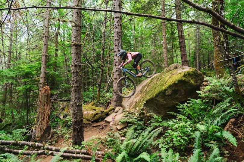 A person riding a bike over a rock in the woods

Description automatically generated with medium confidence