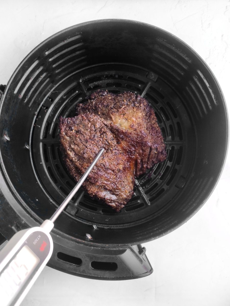 An air fryer effortlessly cooking a delicious ribeye steak to perfection alongside a precise thermometer to ensure ideal cooking temperature.