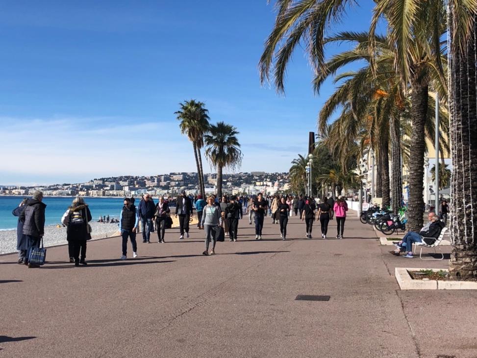 A group of people walking on a sidewalk by a body of water

Description automatically generated