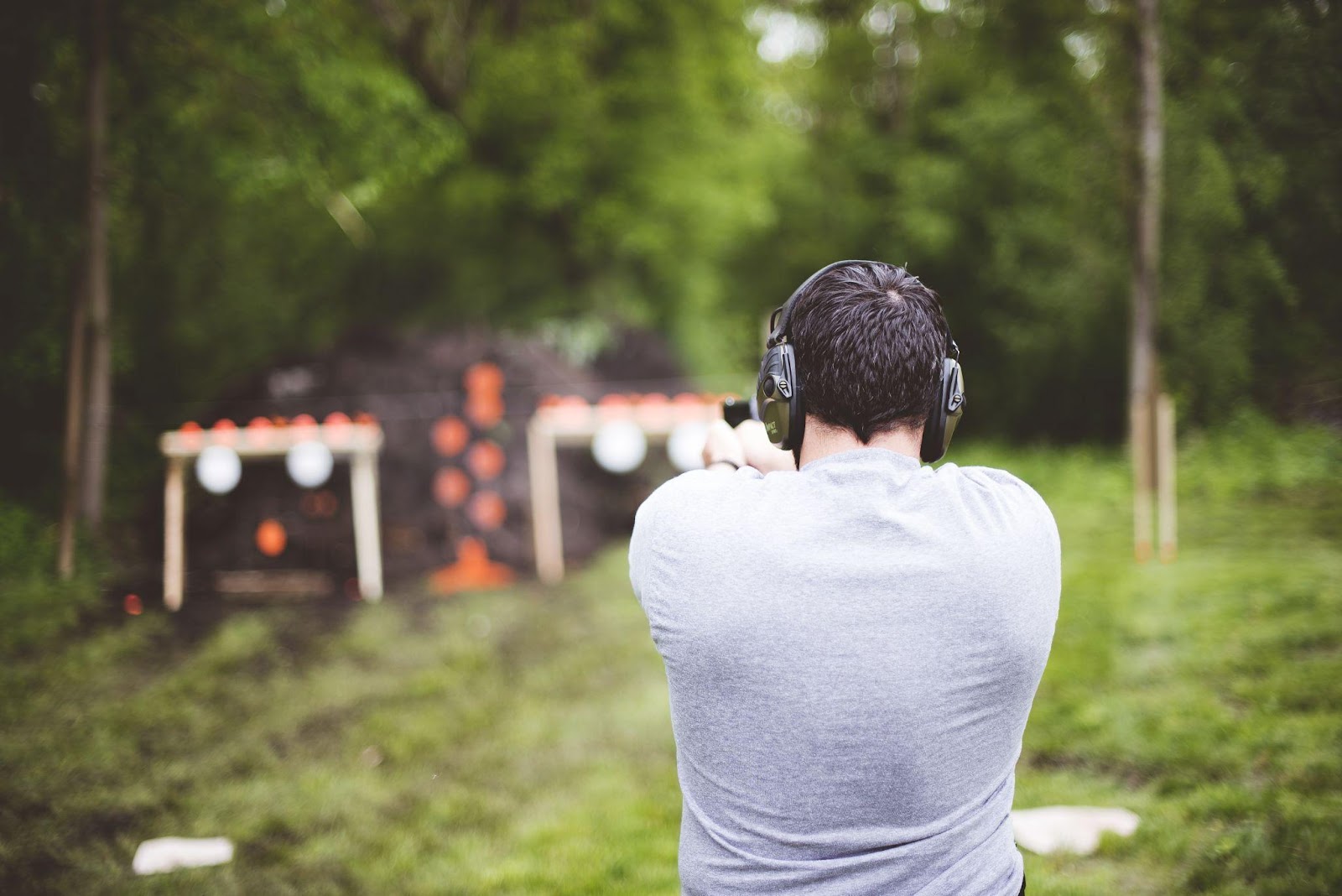 muž v šedém tričku s ochrannými sluchátky na uších střílí na terč