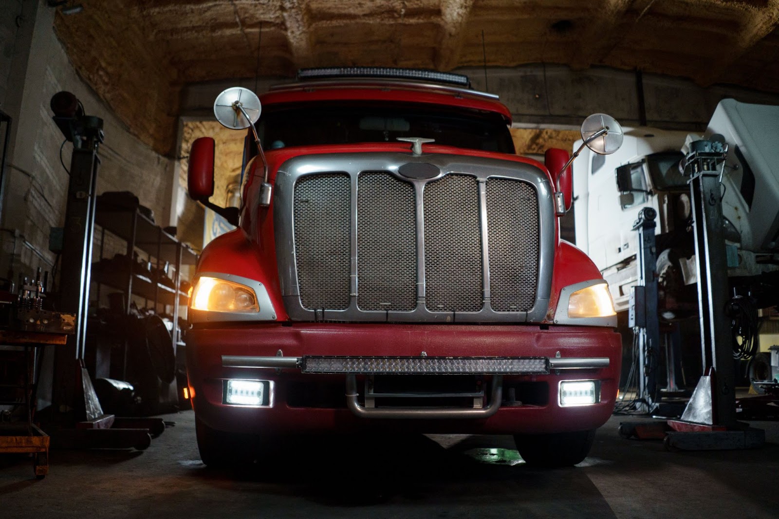A fish-bowl-style photo of a red semi truck in a repair shop