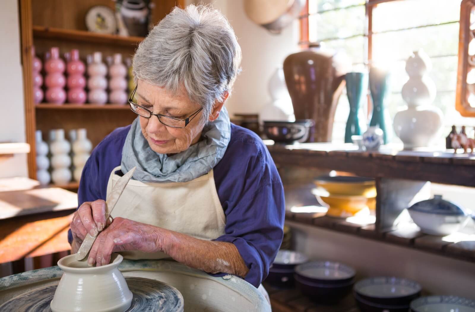 An older adult woman making a pot for her pottery class.