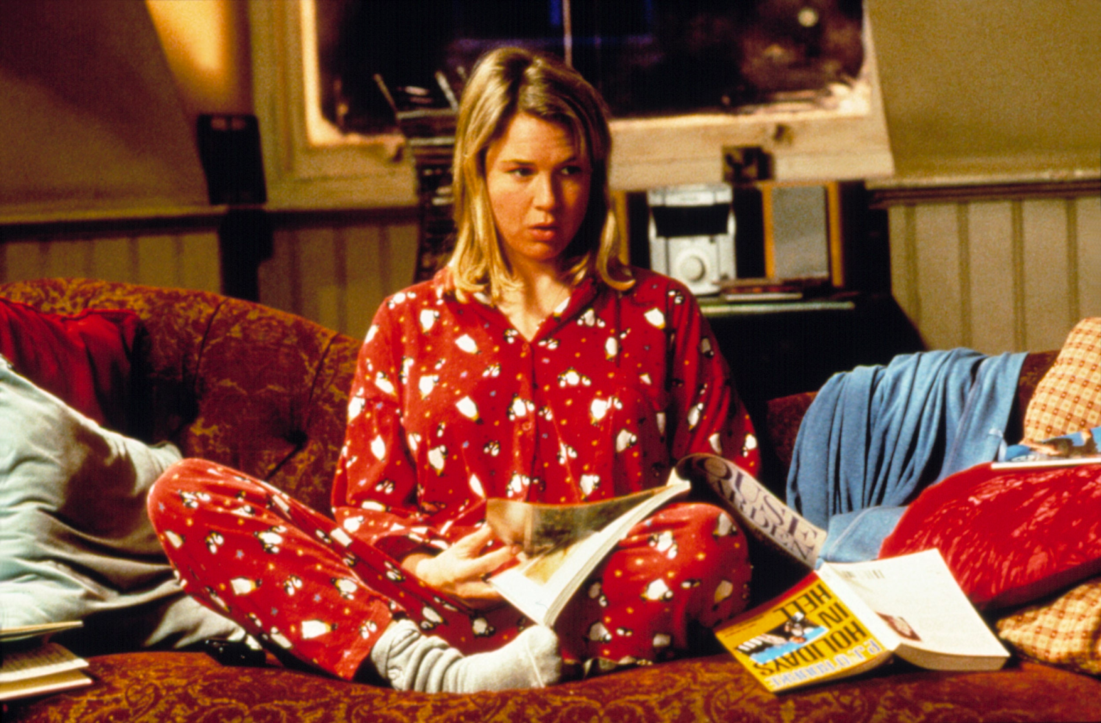 Renee Zellweger's character in Bridget Jones's Diary sits comfortably cross-legged, immersed in a pile of magazines, flipping through them with a mix of curiosity and contemplation, reminiscent of the cozy and heartwarming scenes found in the best comfort Christmas films. Her search through the magazines reflects a quest for guidance or inspiration, adding to the film's relatable charm.