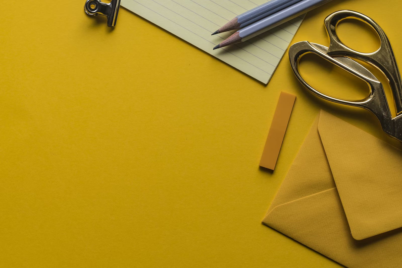 an overhead shot of scissors, pencils, and paper on a yellow sheet of paper