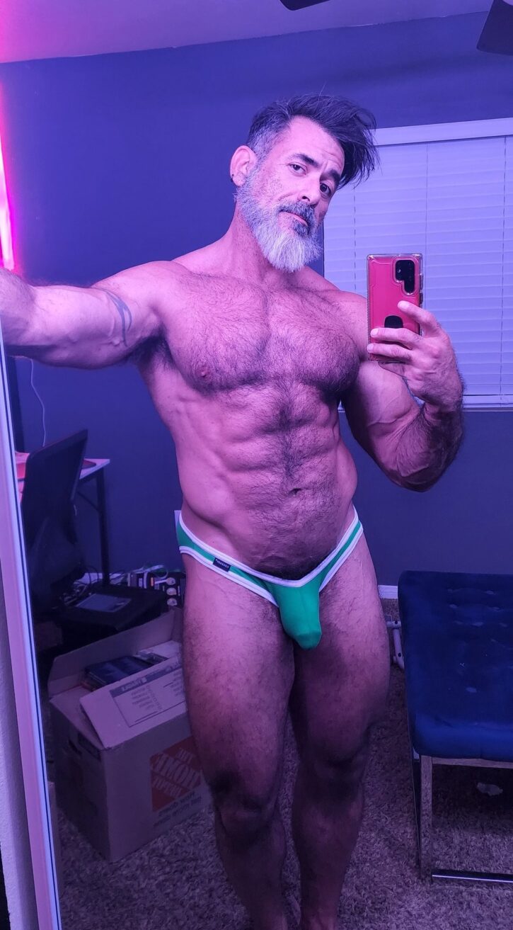 Lawson James posing in a dark room in fron tof the mirror in a tiny little green athletic jock strap