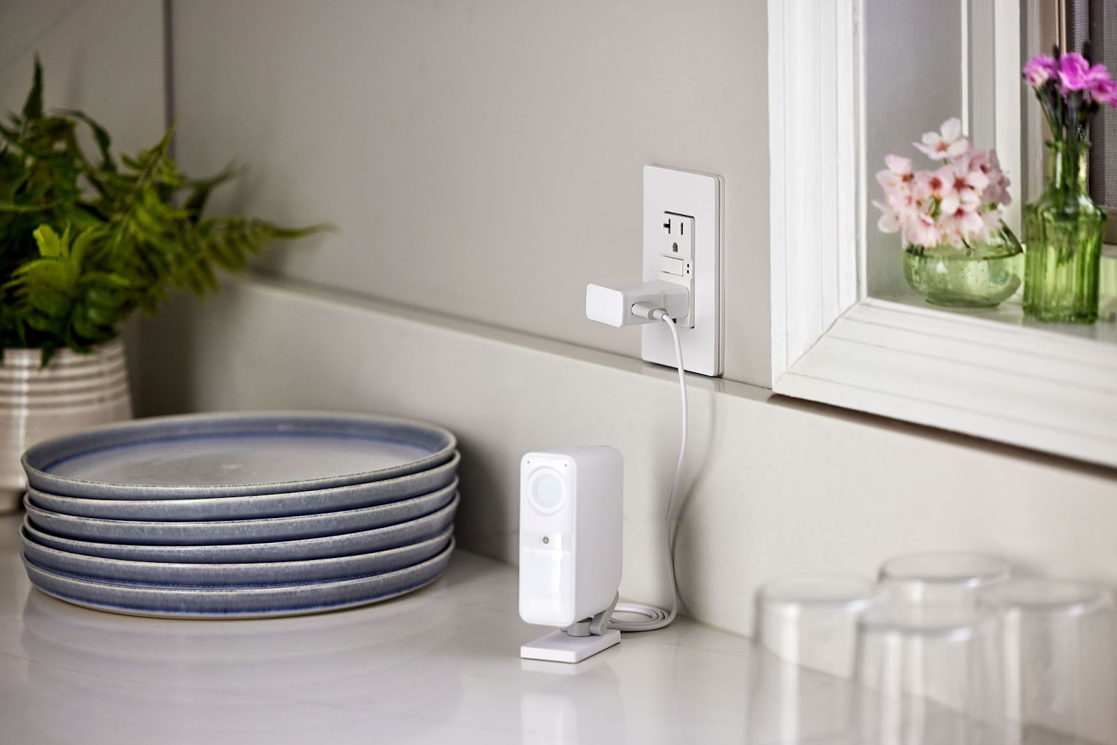 Smart Alarm Indoor Camera plugged into wall outlet on kitchen counter.
