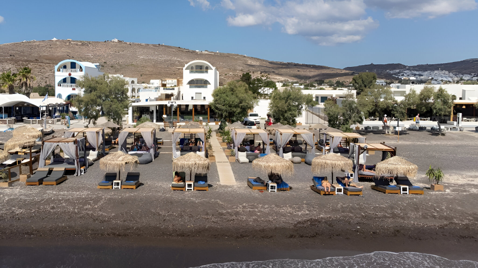 Sun loungers with umbrellas of a beachfront rental in Santorini. 