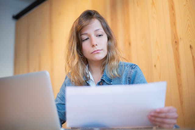 A person sitting in front of a laptop and holding a document