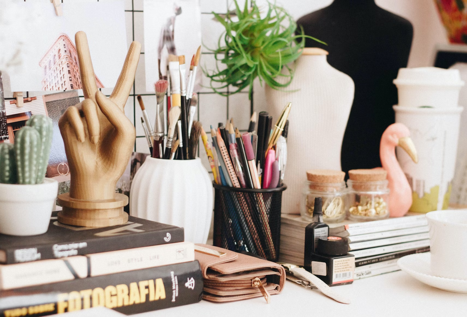 a desk with several books, sketchbooks, pencils, plants, and knick-knacks with a hand statue making the peace sign