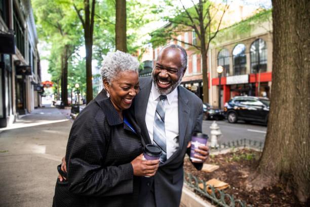 senior couple strolling through downtown area holding coffee - loving couple walking stock pictures, royalty-free photos & images
