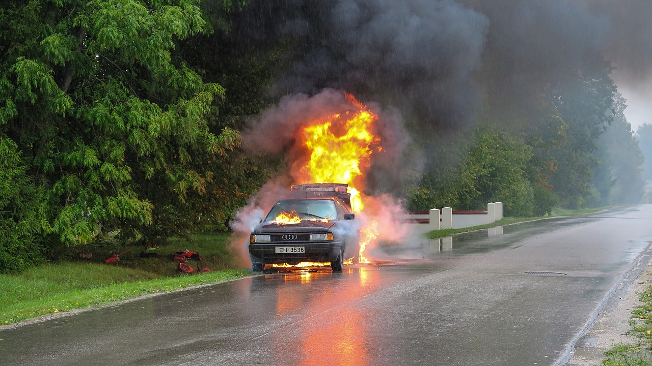 a burning car on the side of a road surrounded by trees