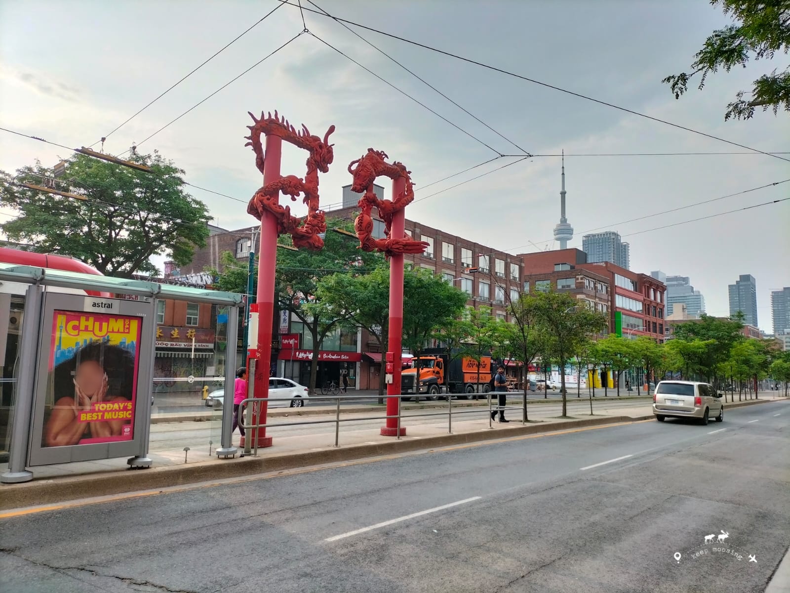 A bus stop in China Town with a typical Chinese red door. The CN Tower stands out in the background.