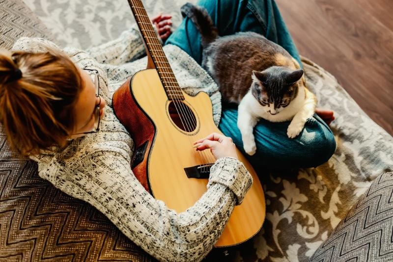 mujer tocando la guitarra con gato en su regazo