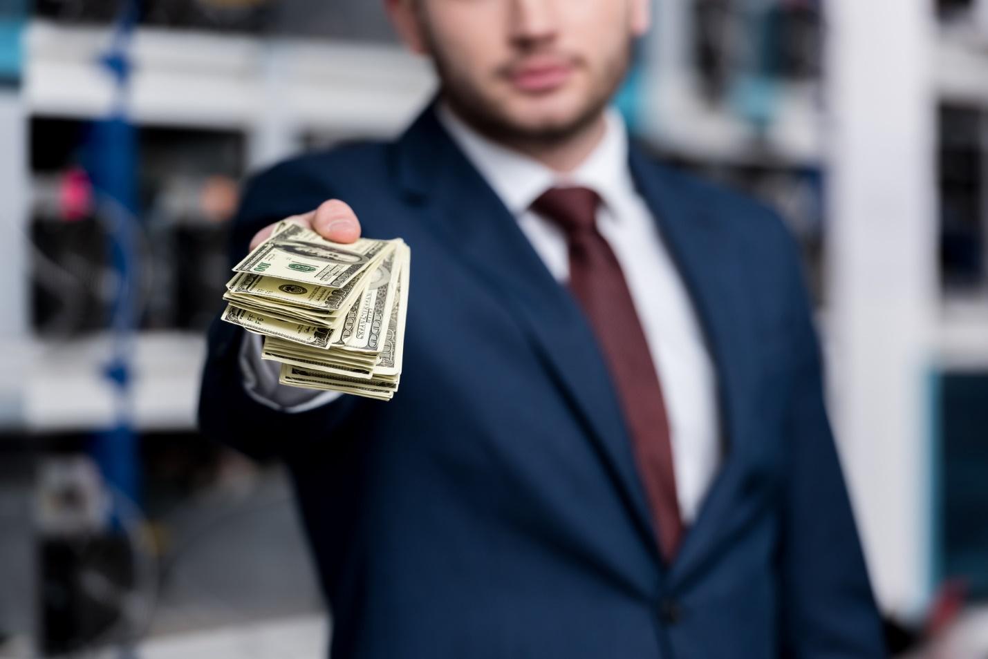 A person in a suit holding money

Description automatically generated