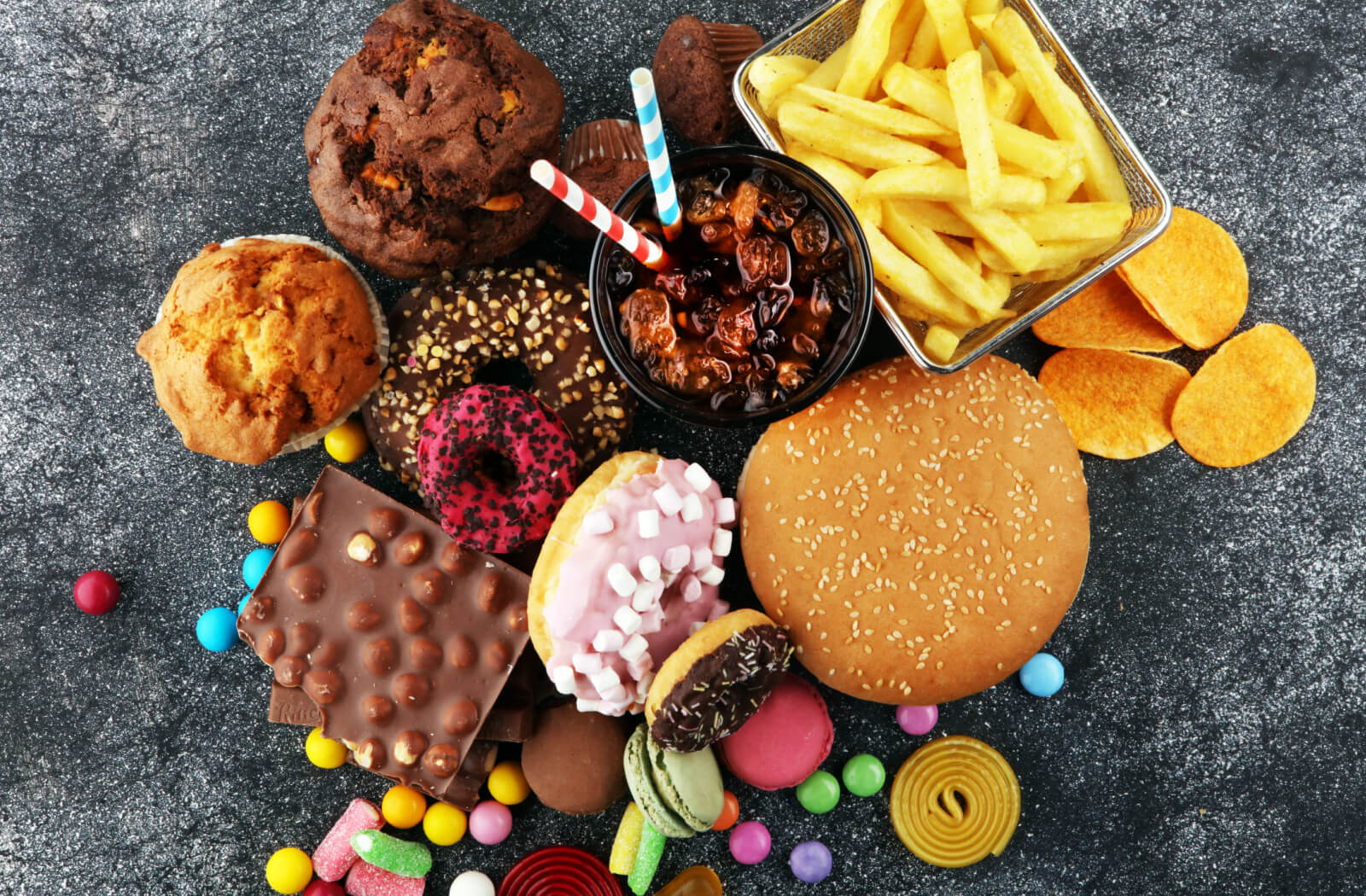 An assortment of junk food including donuts, soft drinks, and fries on a grainy backdrop.