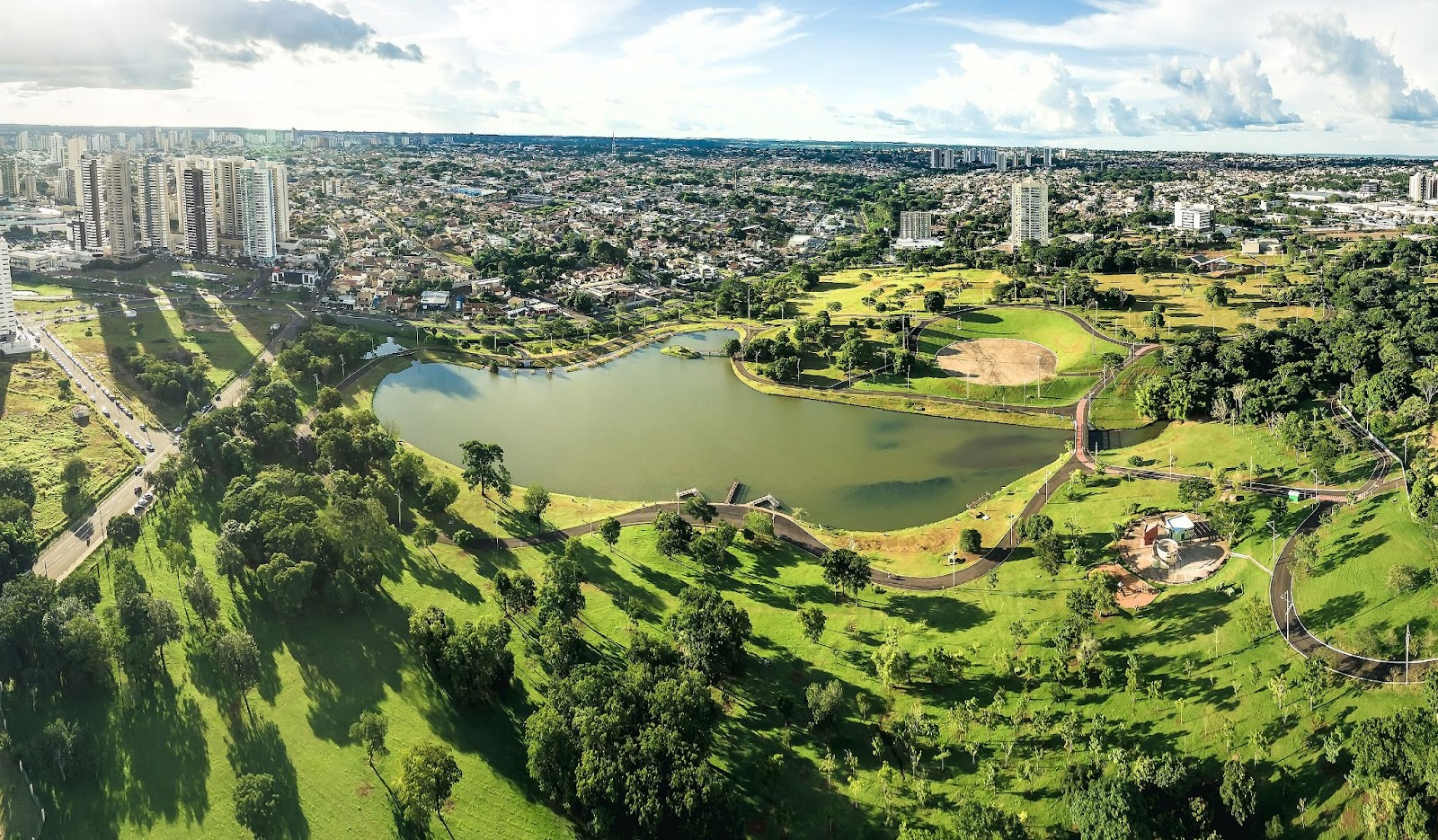 Vista aérea do Parque das Nações Indígenas. Grande área verde com gramado, árvores e lago verde