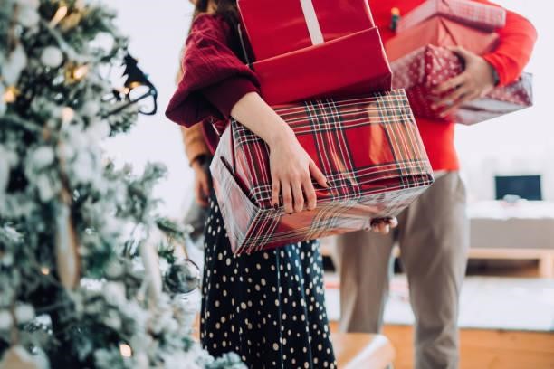 Close up of young Asian woman and man at the back holding a pile of wrapped Christmas presents standing next to Christmas tree preparing for a Christmas party Close up of young Asian woman and man at the back holding a pile of wrapped Christmas presents standing next to Christmas tree preparing for a Christmas party Family Gift stock pictures, royalty-free photos & images