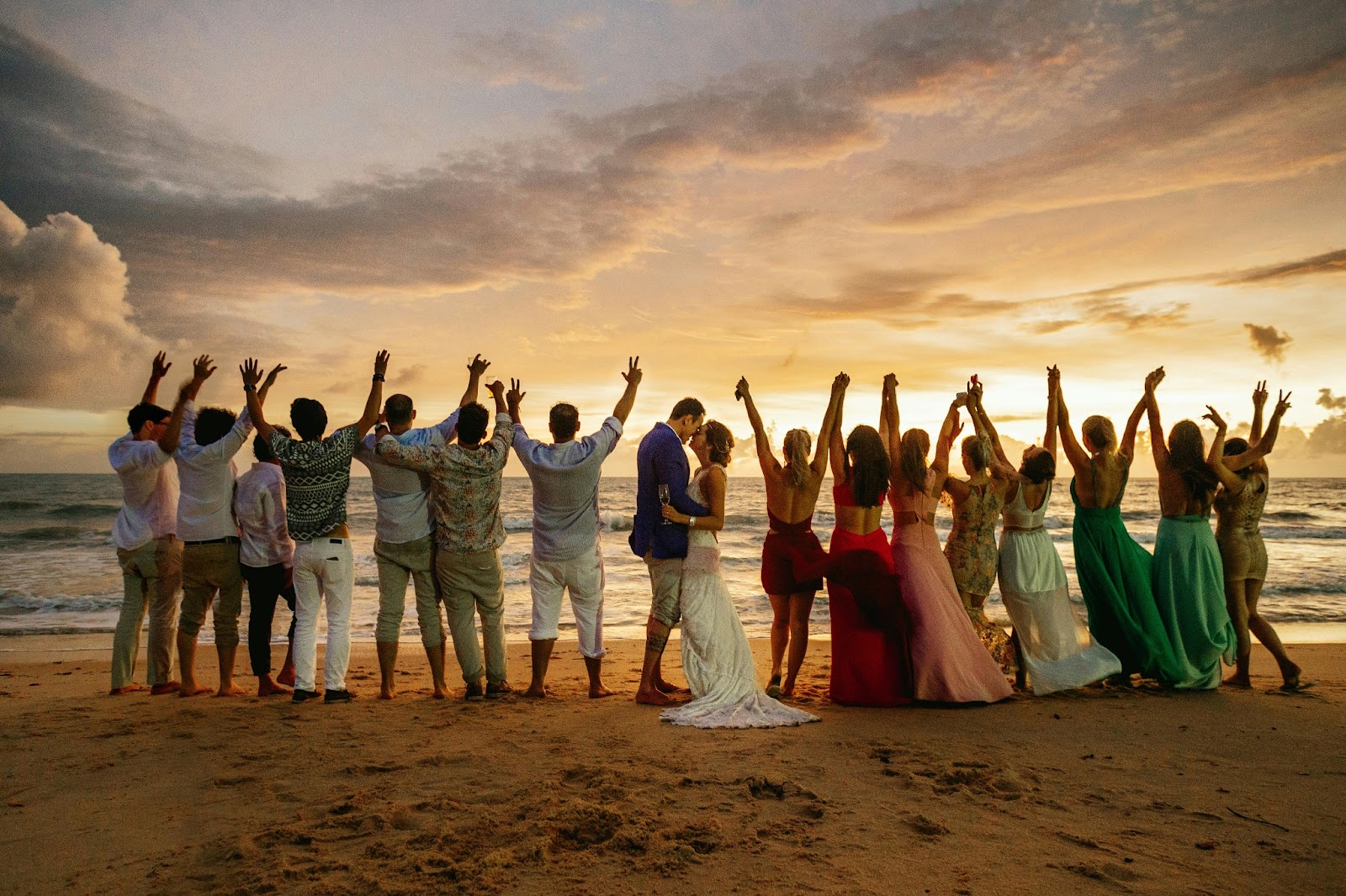 A group of guests laughing and celebrating the married couple on the beach at night.