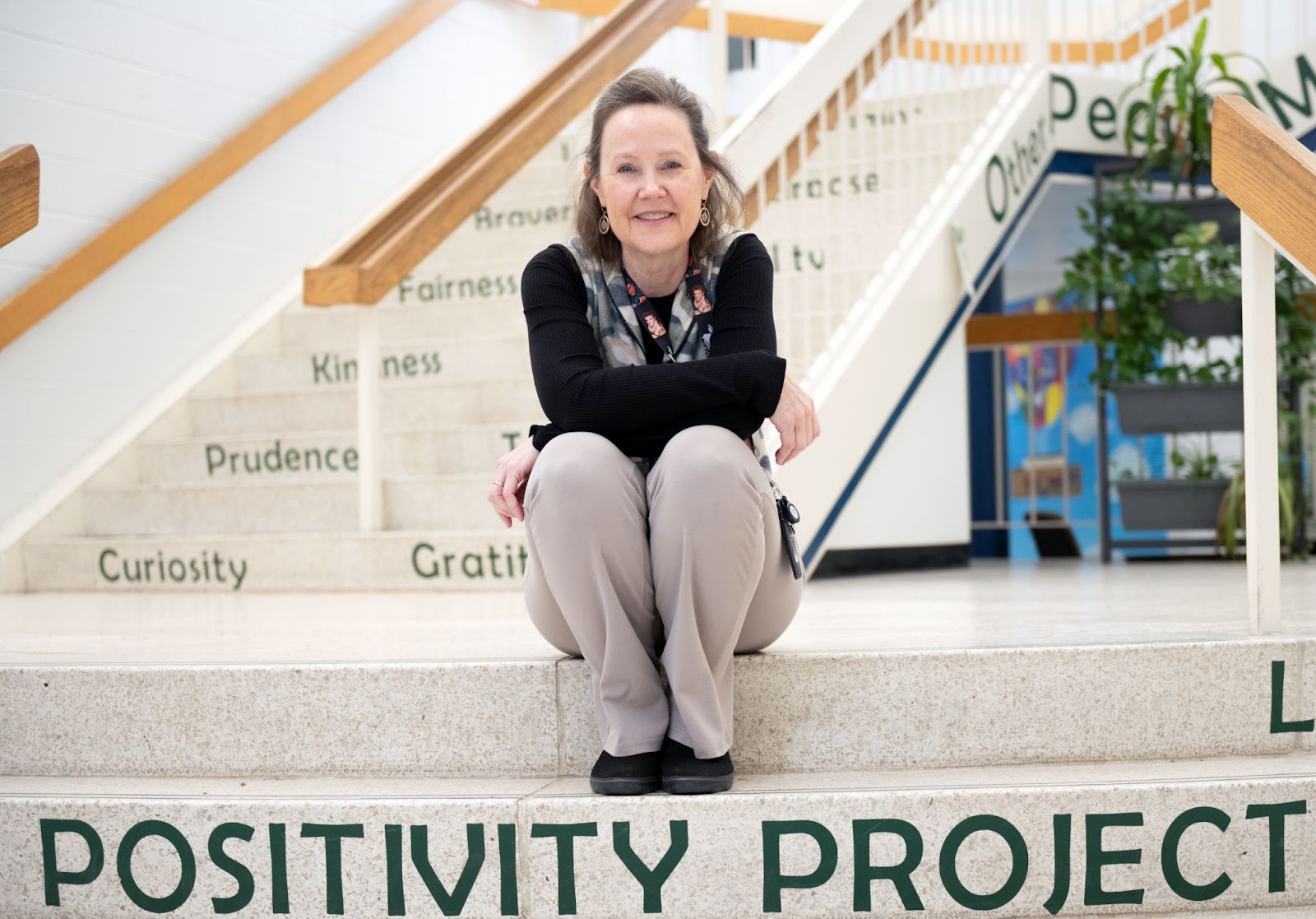 A counselor sits on steps, upon which are written "Positivity Project"