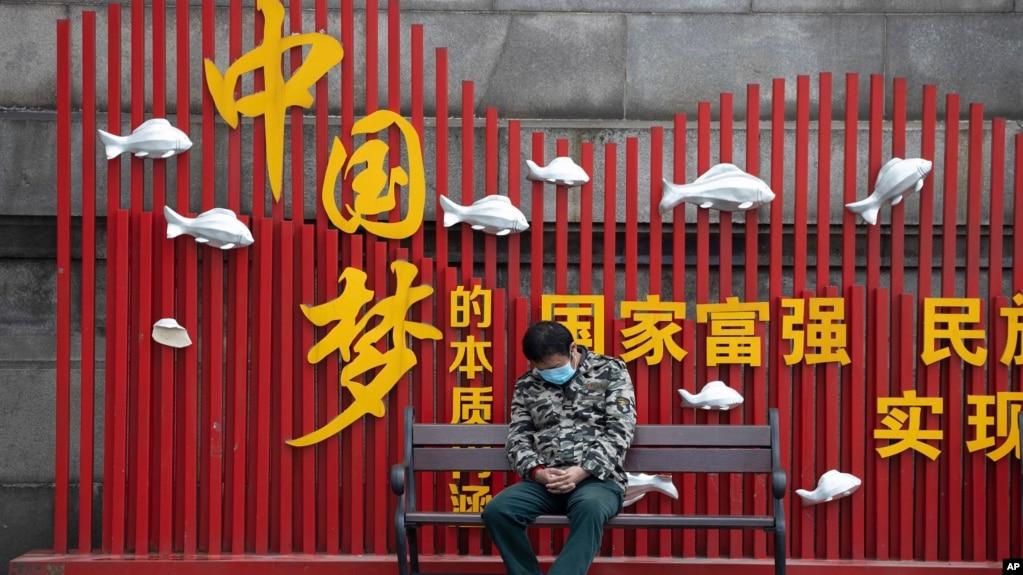 资料照:一名戴着口罩的男子在武汉街头一个中国梦的政府宣传牌下打盹。(2020年4月8日)