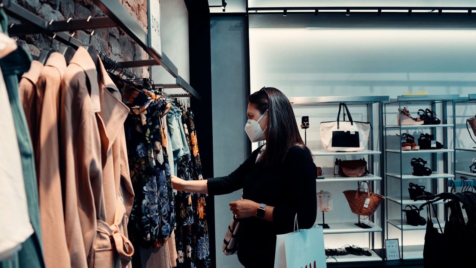 A woman in a retail store checking on the dresses while holding a paper bag