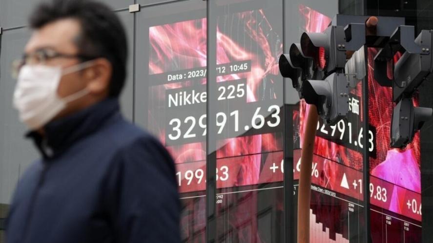 A person walks in front of an electronic stock board showing Japan's Nikkei 225 index at a securities firm Tuesday, Dec. 12, 2023, in Tokyo.