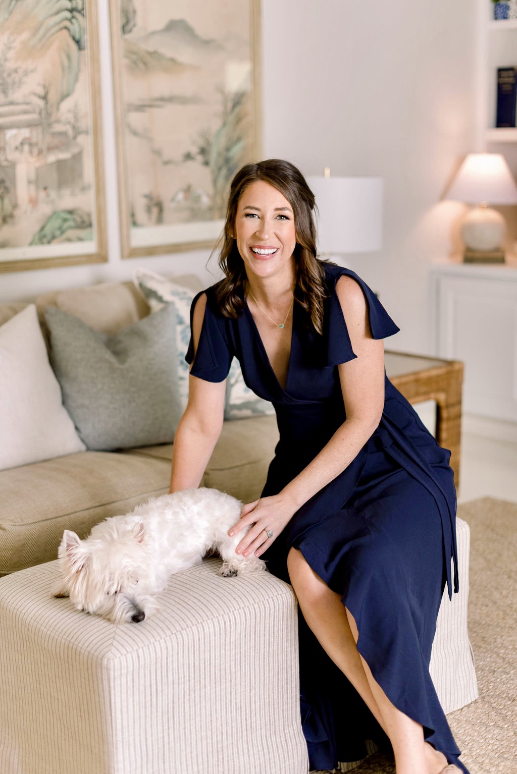 Photo of Sally sitting on the ottoman in her living room, smiling warmly with her dog lying next to her.