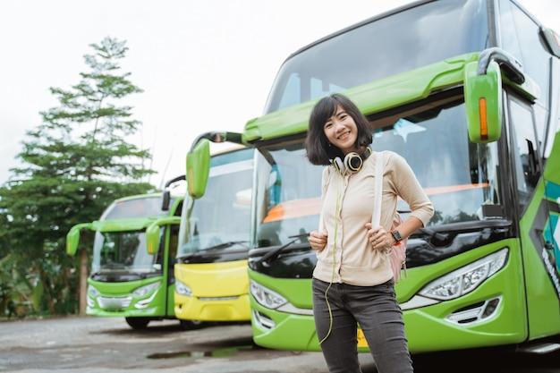Photo an asian woman is standing in a backpack and headphones smiling against the bus