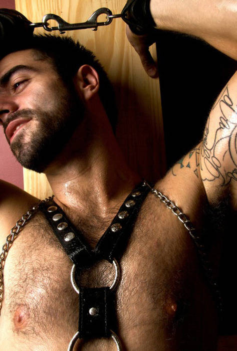 male wearing BDSM harness and chains smiling and lying down on a wooden plank