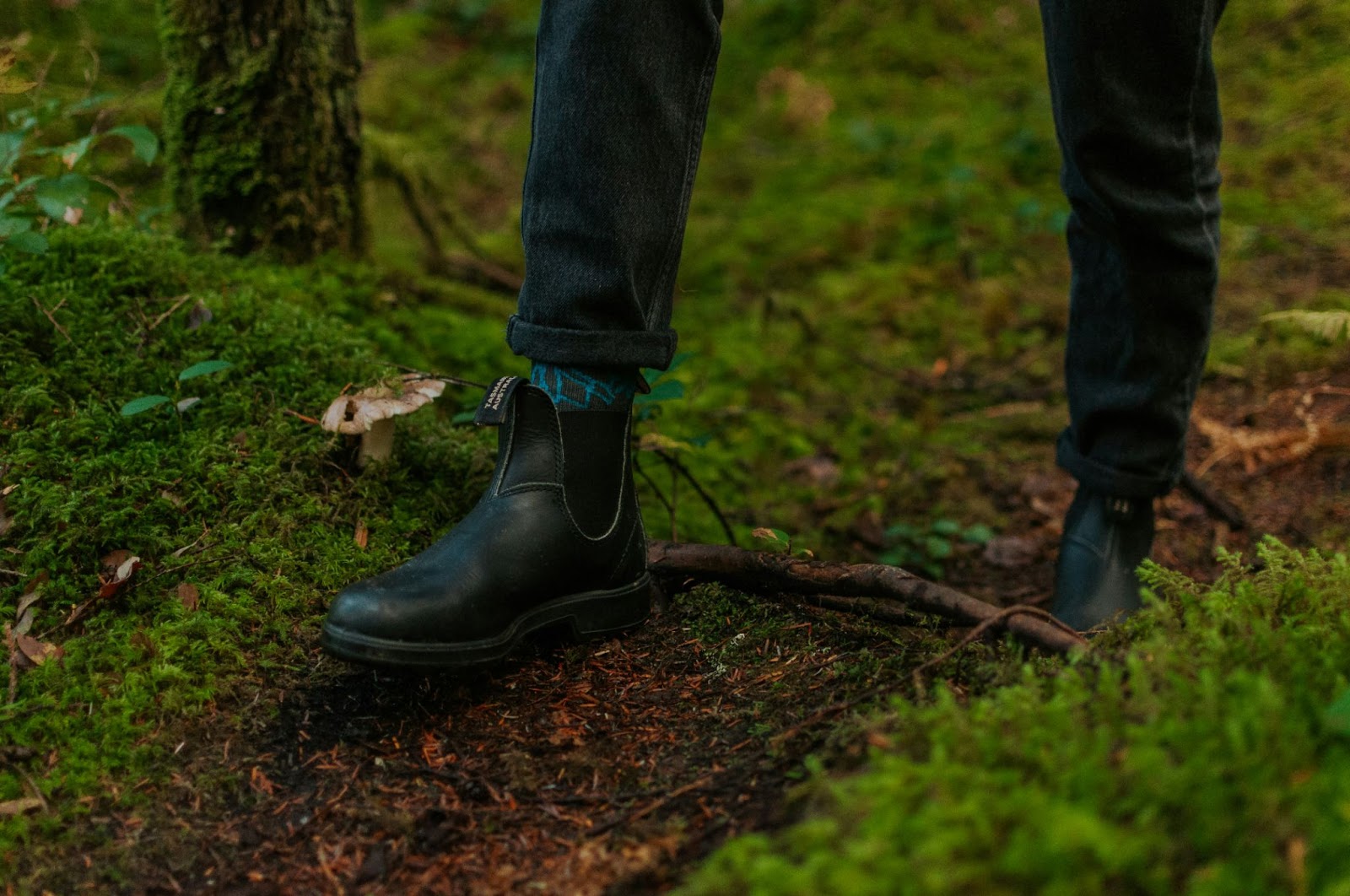 a close up of the forest floor and someone wearing boots and jeans, walking down a dirt path