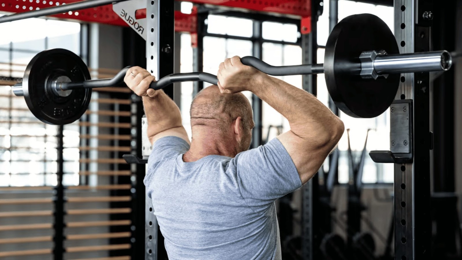 man performing overhead tricep extensions with rackable rogue ez curl bar