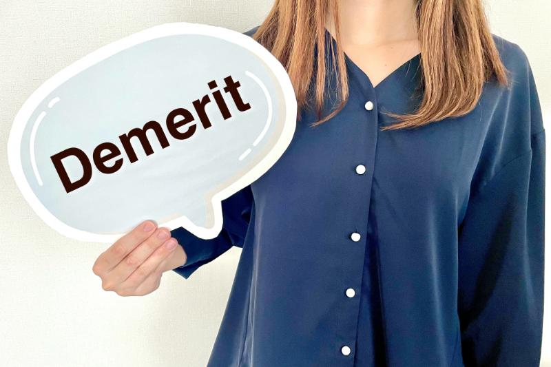 「Demerit」と書かれた吹き出し型の紙を掲げる女性