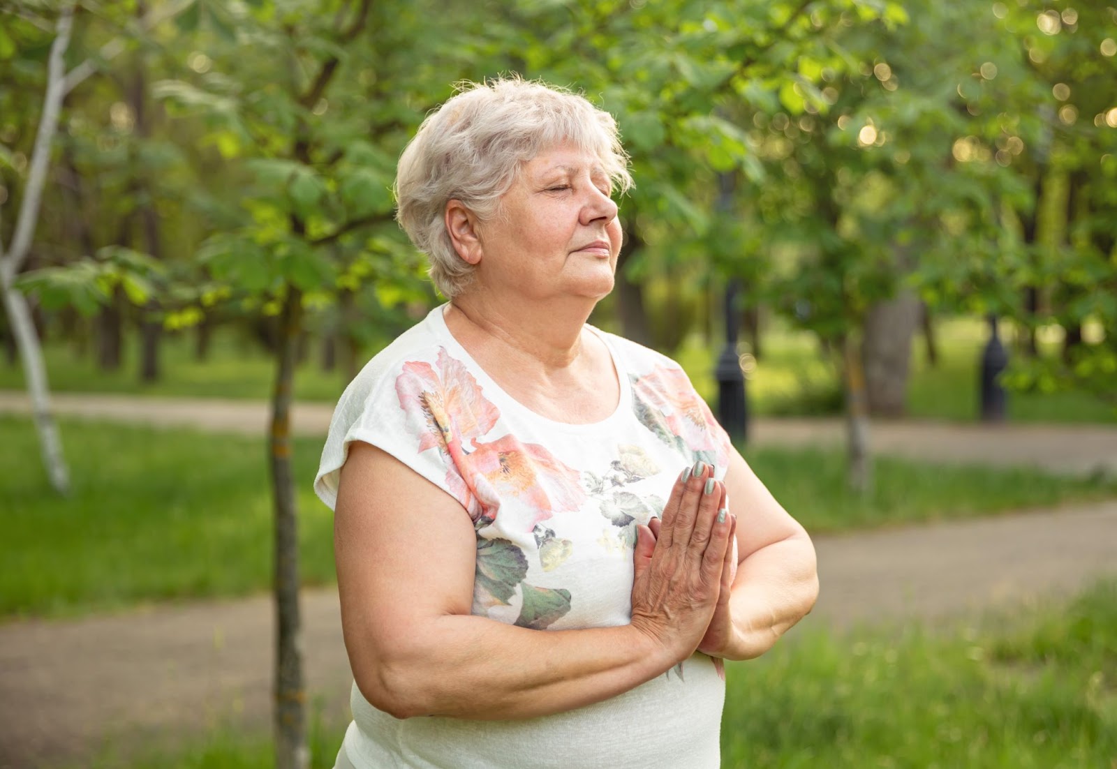 Senior woman in nature practising gentle breathing and meditation with her hands together in front of her
