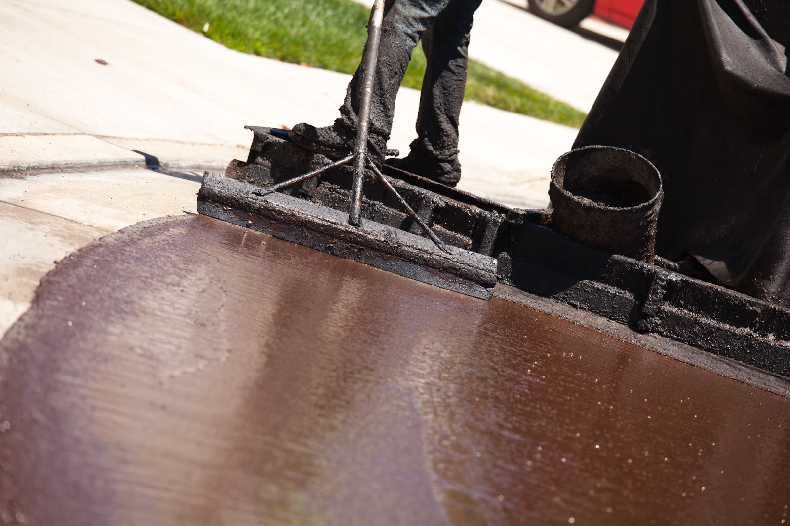 A close-up view of a road worker's legs and feet in black pants and shoes, resurfacing the street, demonstrating asphalt pavement maintenance.