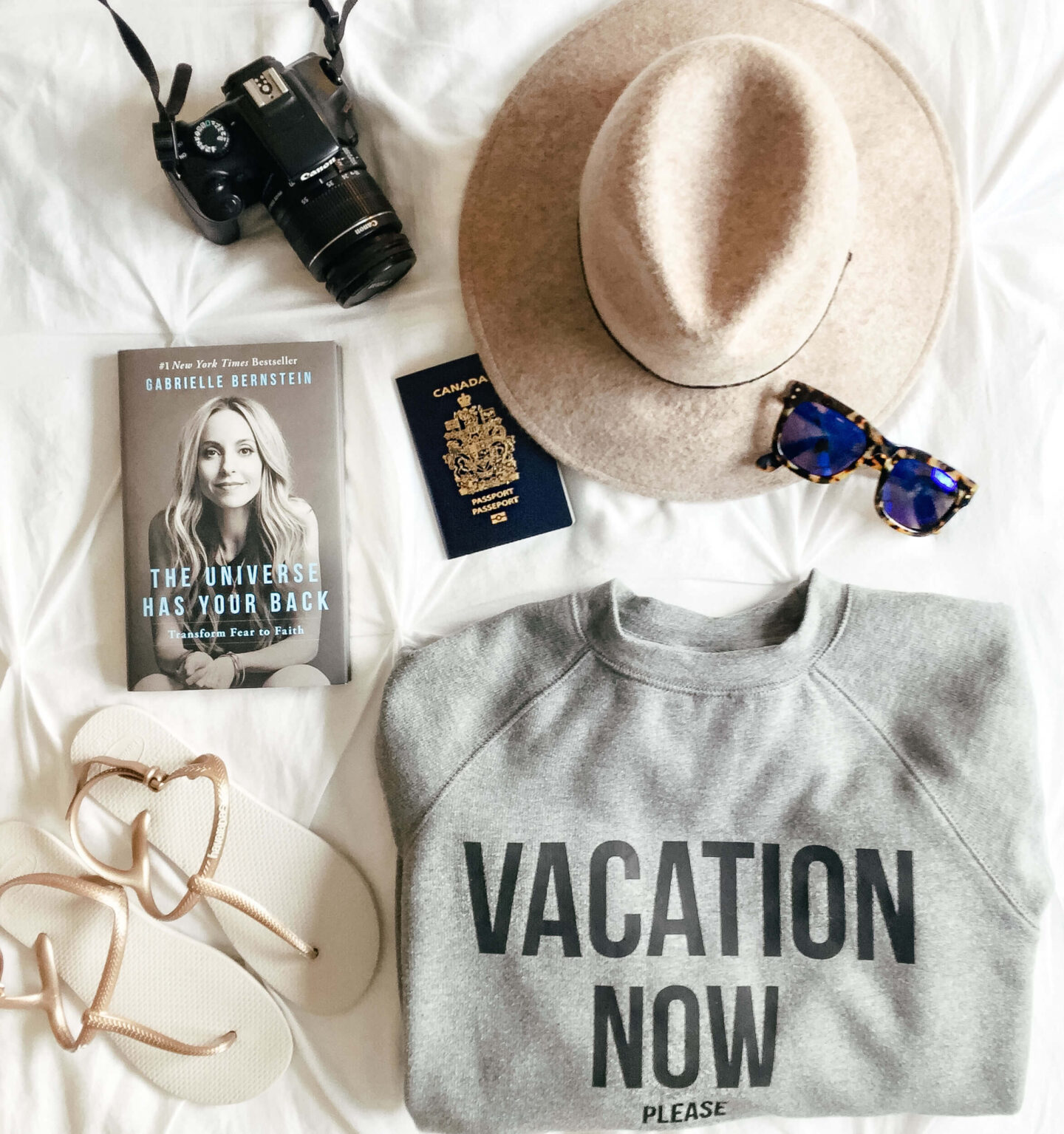 A flat lay from a girl packing up for Palm springs. Items include a hat, book, passport, sunglasses, sandals, and camera.