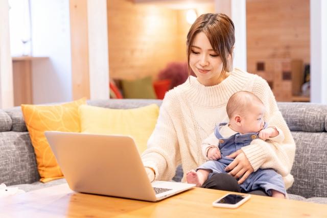 赤ちゃんをわきに抱え、パソコンを操作する女性の写真