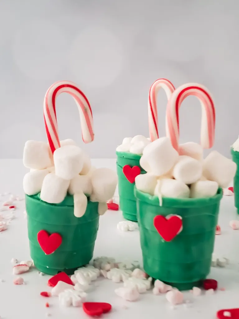 grinch cocoa cups with marshmallows and candy canes red hearts on green cups